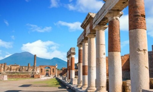 A stone gate and ruin of the city. Behind it is blue sky and big mountains. It is situated in Pompei, Italy in Europe.